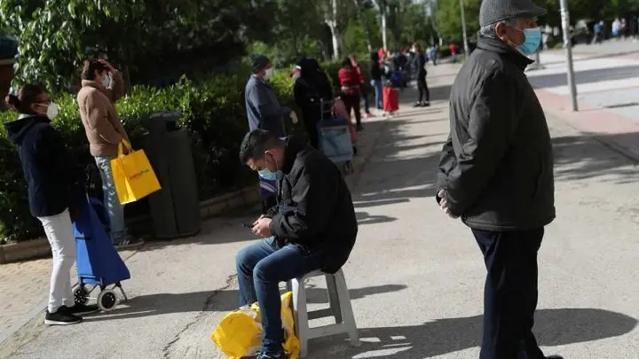 Gente hace cola para recibir alimentos donados en el barrio de Aluche, Madrid.