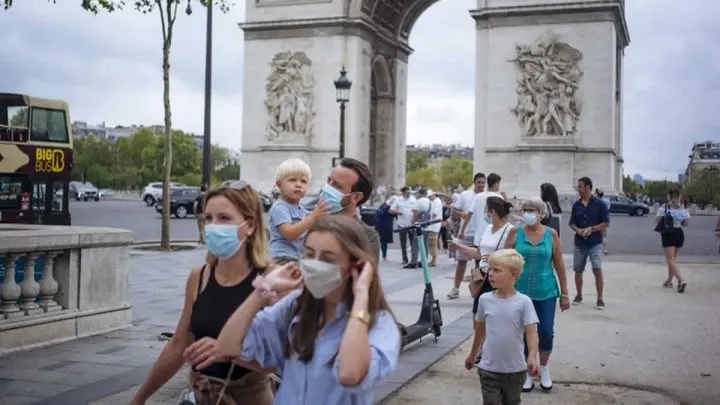 Una familia con mascarillas de protección camina por la Avenida de los Campos Elíseos, con el Arco de Triunfo de fondo, en París
