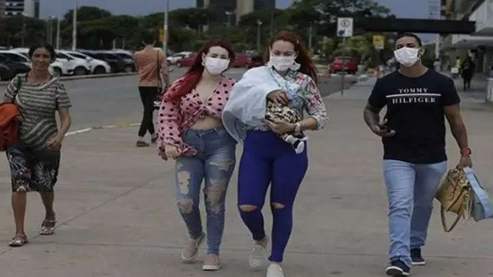 Latinoamericanos caminan por una calle usando mascarillas