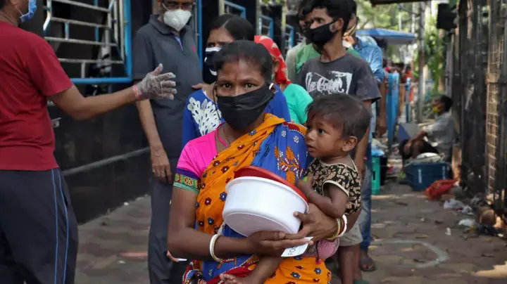 Una mujer con mascarilla carga a un niño en India