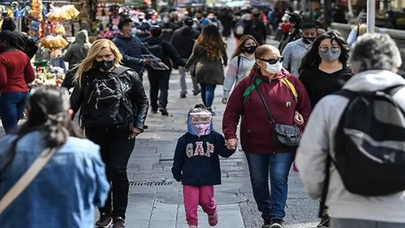 Niña con mascarilla de mano de su mamá en un lugar público.